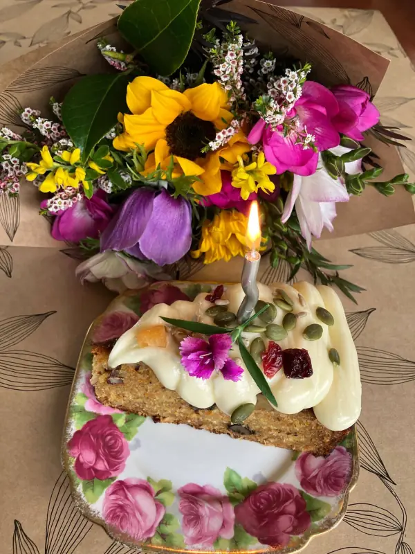 Birthday cake slice in front of a bright bunch of sunflower, tulips and pink blooms