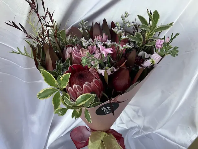 Wrapped bunch of proteas and variegated foliage with a Foraged Flora sticker and ribbon