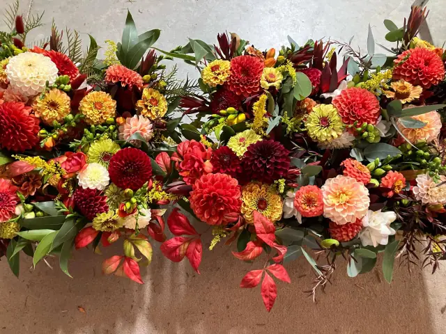 Autumnal table arrangement of dahlias, zinnias and foliage in reds, oranges and golds