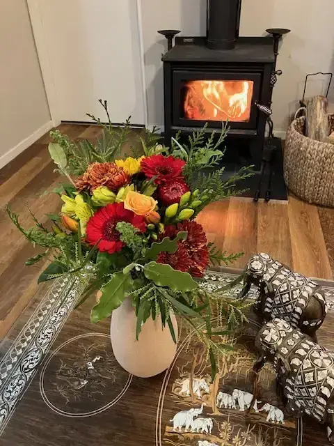 Red, orange and yellow gerbera arrangement beside a wood burner