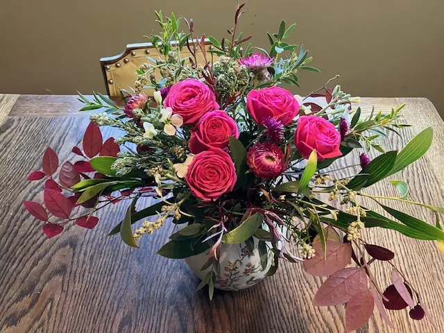 Bright pink roses in a vase on a wooden table with autumn foliage