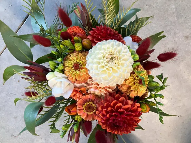 Close-up of a wild bunch with a white dahlia, orange zinnias and burgundy bunny tails