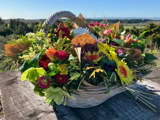 A full wicker basket of mixed seasonal flowers against a sunny Wairarapa landscape