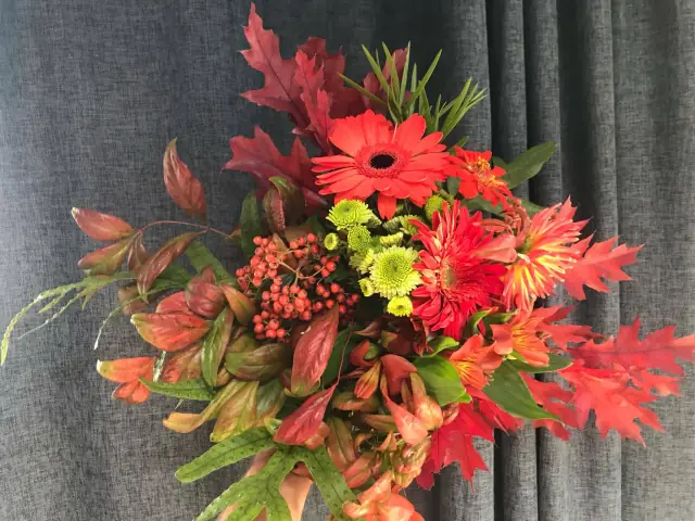 Hand-tied bunch of red gerberas, lime chrysanthemums, berries and autumn oak leaves